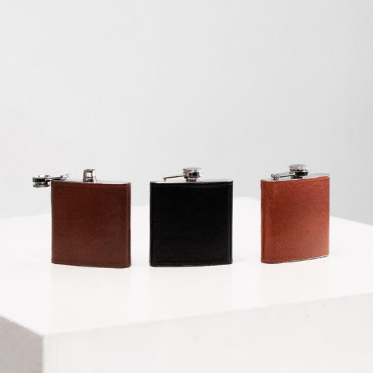 A group of leather-covered flasks, including a black flask with a metal cap and a brown flask with a metal handle, from the Men In Style store.