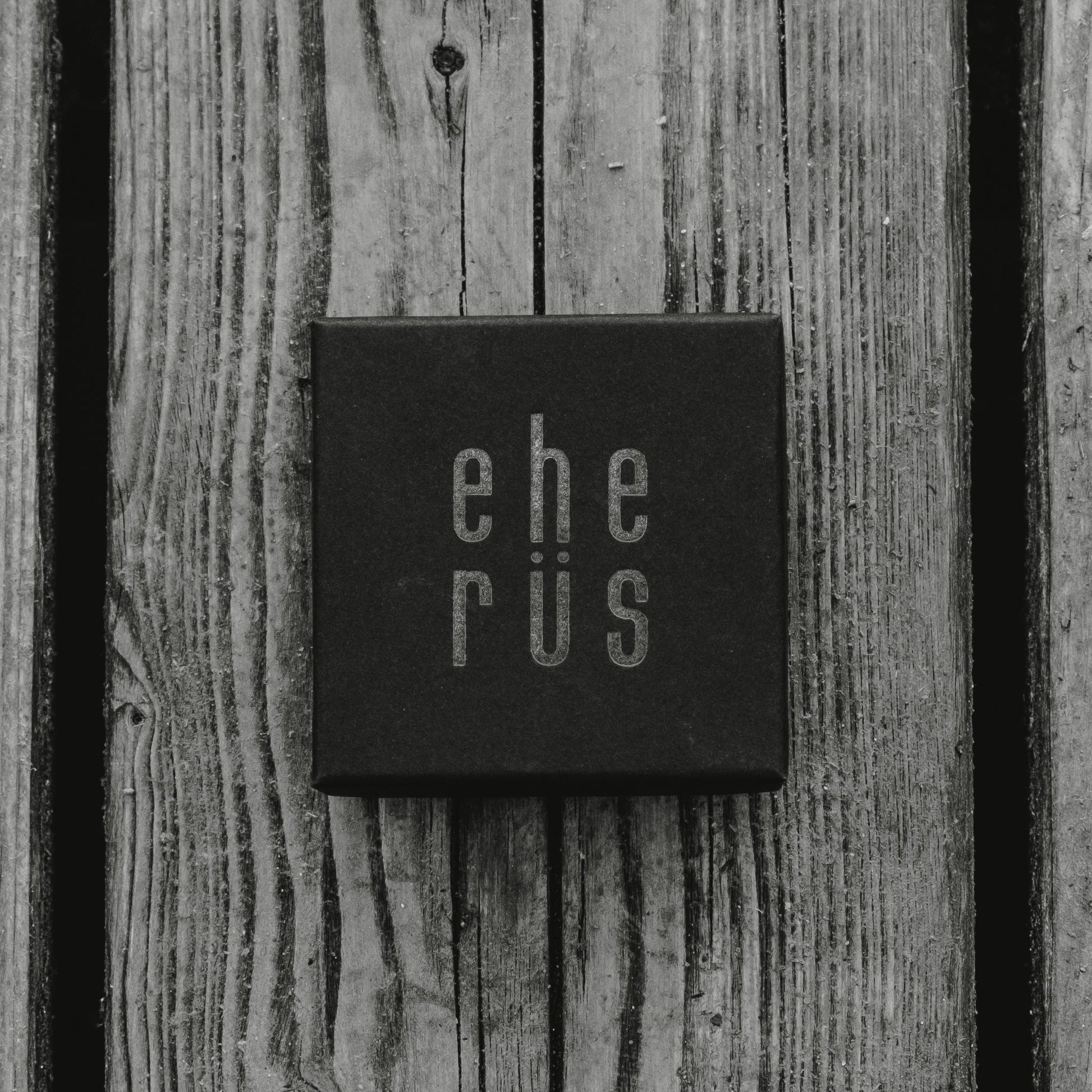 Square cufflinks made of dark trout leather, presented in a black gift box on a wooden surface. Unique fish scale pattern, size 1.7 cm.