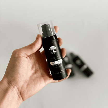 A hand holding a black bottle of Aftershave Balm for Men 30ML, providing a light, refreshing fragrance. Crafted with hyaluronic acid, oat protein, coconut water, aloe, and allantoin to moisturize, tighten, and soothe skin irritations after shaving. Experience irresistibly smooth and soft skin with this nourishing balm from Men In Style.