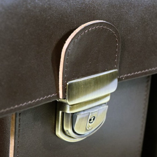 A close-up of the Genuine Thick Leather Briefcase - Dark Brown from Men In Style. Crafted with durable, vegetable-tanned leather, this accessory exudes timeless elegance. Features include a main compartment with laptop and notebook pockets, front pockets, and an adjustable shoulder strap. Designed and produced in Europe with meticulous craftsmanship.