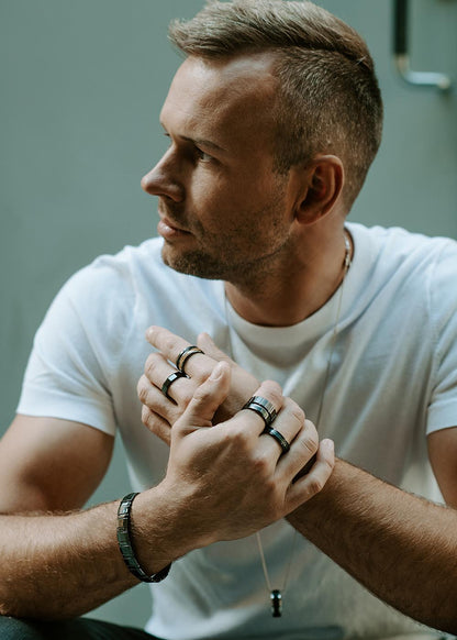 A close-up of a man's hand wearing the Men's ring Leiw made of black high-quality ceramics, with silver rings and a bracelet.