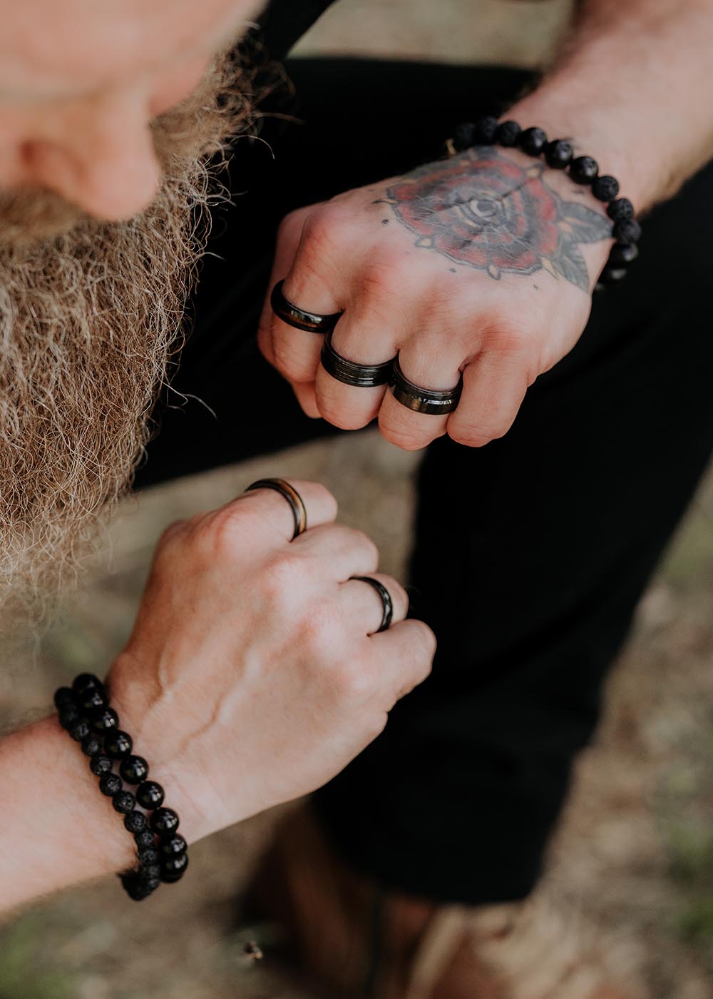 A close-up of a man's hand with a black ceramic men's ring, showcasing intricate tattoos, rings, and bracelets.