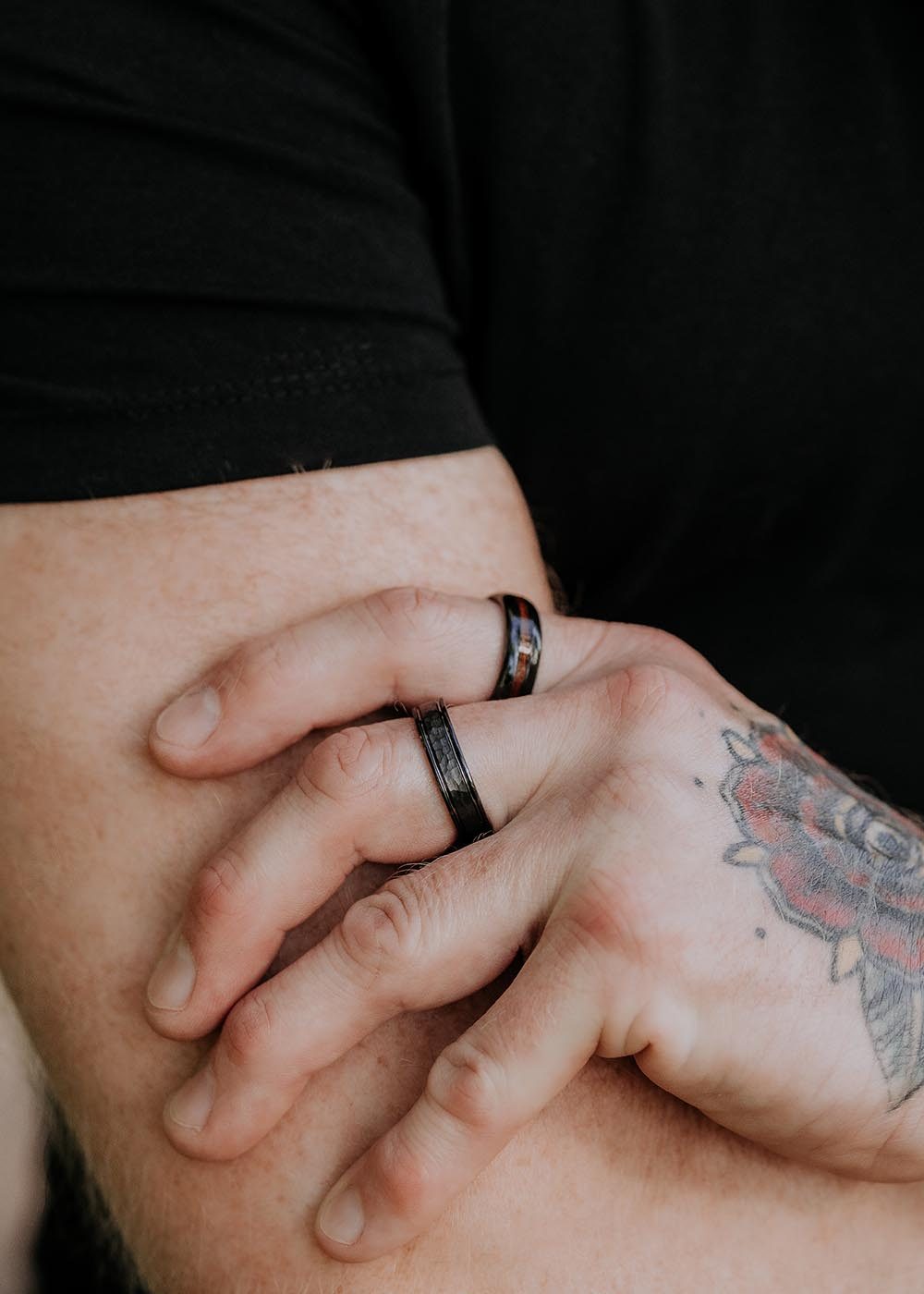 A close-up of a person's hands with Men's ring Rajona, showcasing tattoos, rings, and black high-quality ceramics.