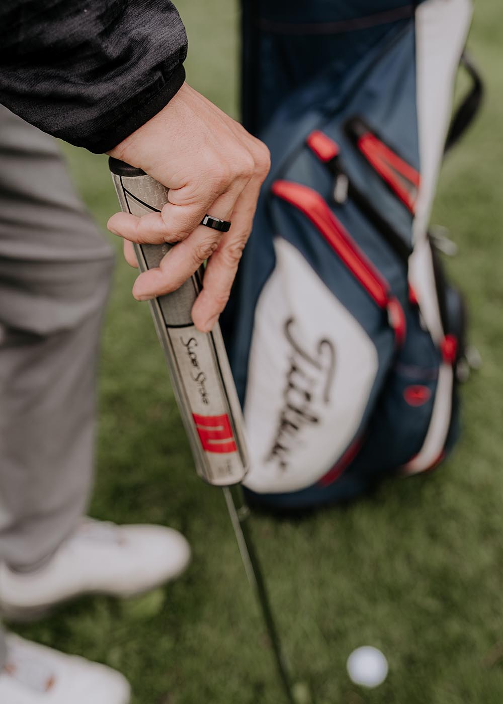 A person holding a black ceramic men's ring with a golf club in the background.