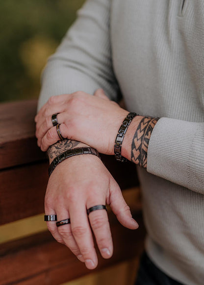 A person wearing the Trey Bracelet for Him, a black ceramic accessory with rings, bracelets, and a tattoo on their wrist.