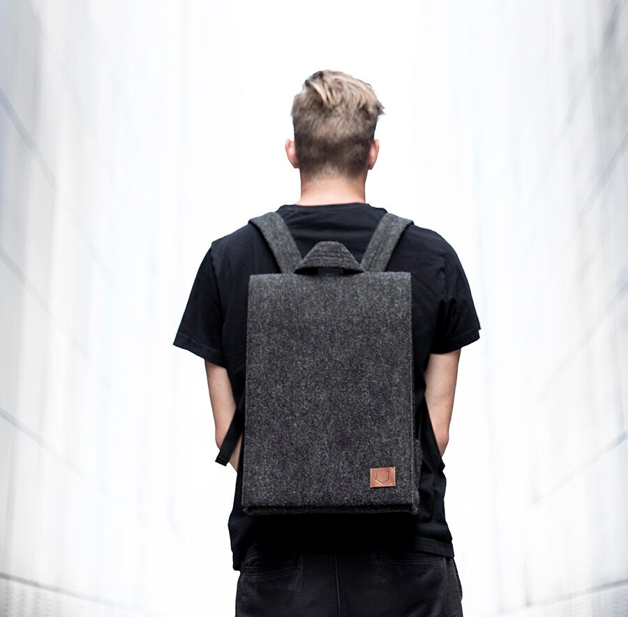 A man wearing a backpack, featuring a minimalist design and durable felt construction. Perfect for a modern, personalized look. Available in various sizes.