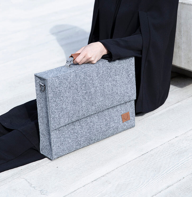 A person holding a grey briefcase with a separate sleeve for up to a 15" laptop - Grey, showcasing sleek and minimalistic style for the modern professional.