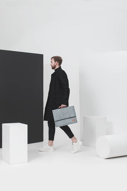 A professional man in a black coat holds a sleek grey briefcase with a separate sleeve for up to a 15" laptop.