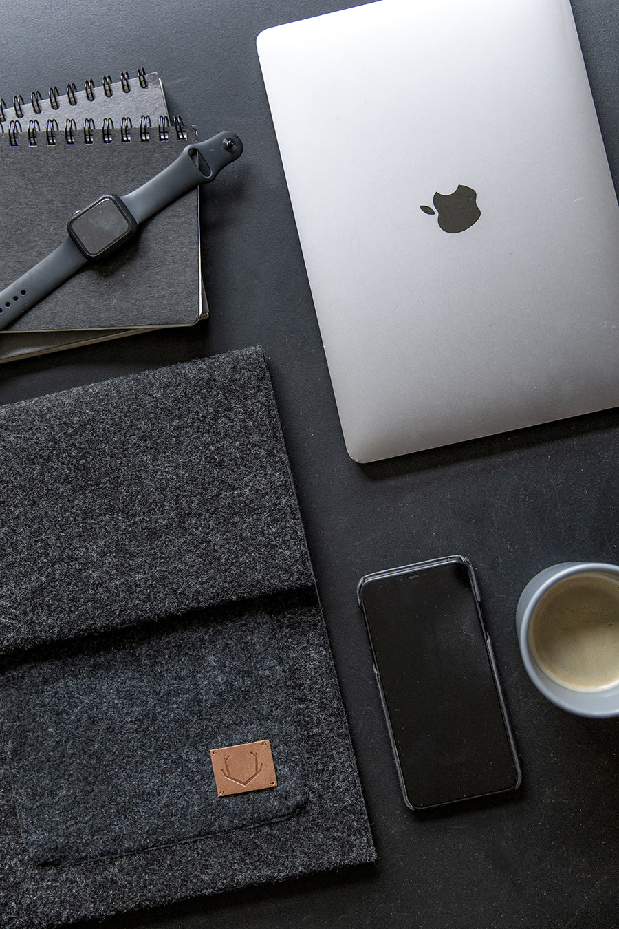 A slim fit envelope sleeve for Macbook Air & Pro - 15" Black, with a laptop and phone on a table, a watch on a notebook, a cup of coffee, and a close-up of a phone and laptop.