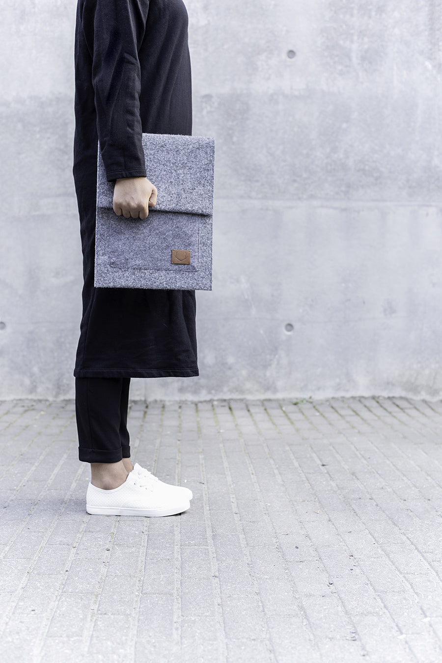 A person holding a grey folder and a grey bag, with a close-up of a white shoe and a black fabric.