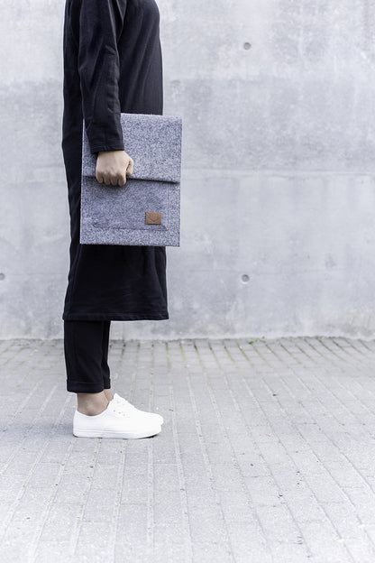 A person holding a grey folder and a grey bag, with a close-up of a white shoe and a black fabric.