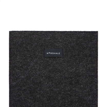 Slim fit sleeve for Macbook Air & Pro - 15" Black: A black square object with a black label featuring a logo. Perfect for professionals and students, it keeps your laptop safe and stylish. Made from durable felt, it offers functionality and style.