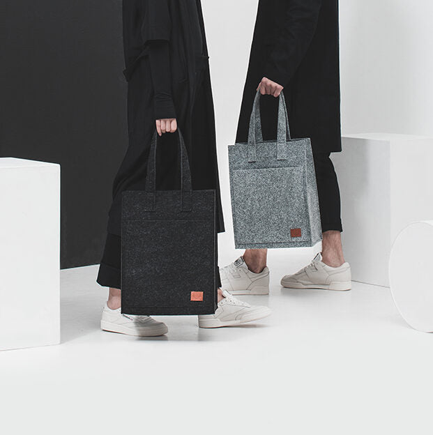 Two people holding bags, including the Tote Bag - Grey from Men In Style. Made from recycled PET felt, weatherproof, and featuring a laptop pocket. Sustainable and handmade in Europe. Spacious and durable for all your essentials.