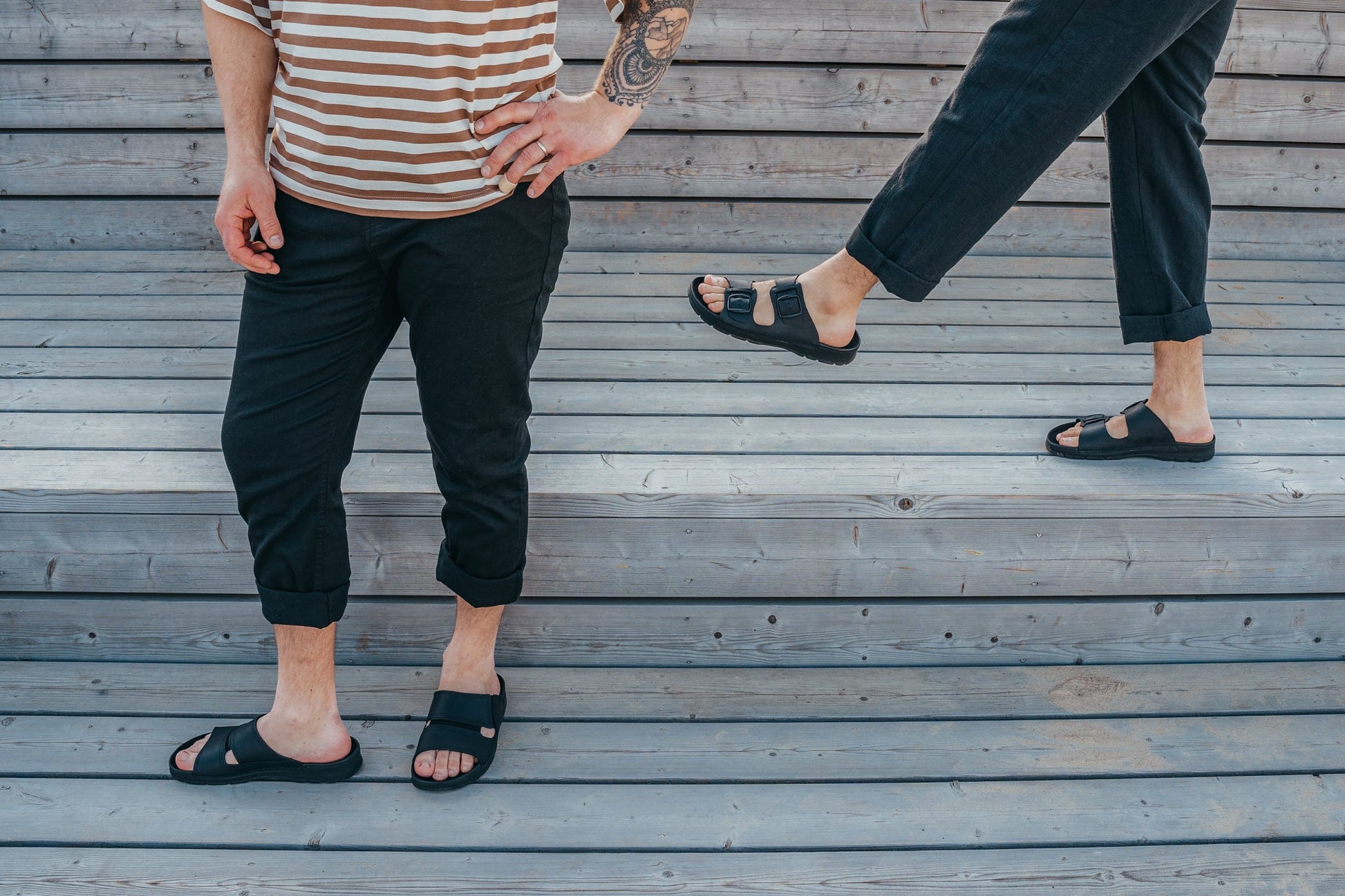 A pair of men wearing Slip-On Leather Sandals with Adjustable Buckle in classic black, offering timeless style and exceptional comfort. Made in Europe with premium leather, these sandals feature adjustable buckle straps for a customized fit and an anatomically supportive insole for all-day comfort. The springy and durable polyurethane (PU) outsole ensures worry-free indoor wear. Experience style and functionality with these versatile sandals from Men In Style.