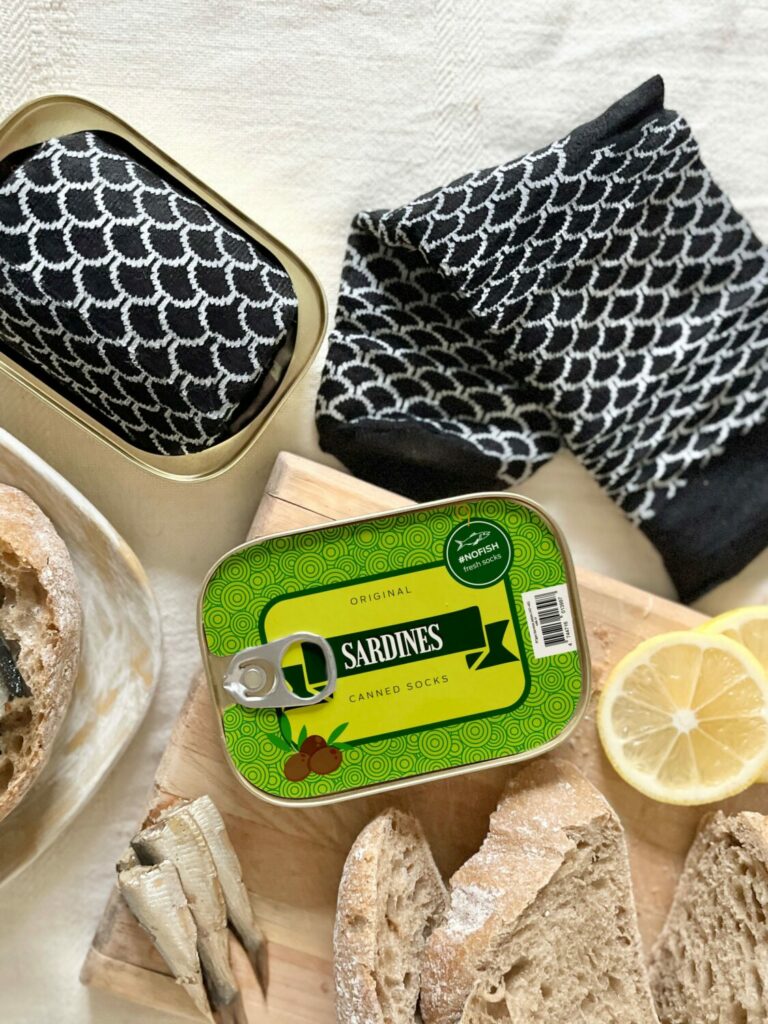 French Sardine Socks in a Can - size 35-46, displayed with a can resembling fish packaging, alongside a lemon and bread, highlighting its novelty and playful design.